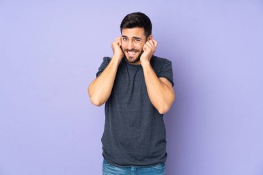 Kafkasyalı yakışıklı adam hayal kırıklığına uğramış ve mor arka plan yüzünden kulaklarını kapatmış.