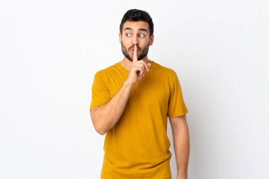 Beyaz arka planda sakallı yakışıklı genç adam sessiz bir jest işareti gösteriyor. Parmağını ağzına sokuyor.