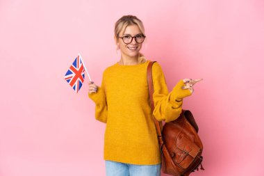 Pembe arka planda izole edilmiş bir Birleşik Krallık bayrağı tutan genç bir Rus kadını işaret ediyor.