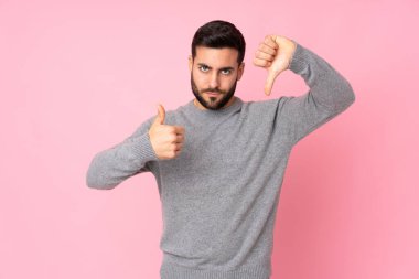 Kafkasyalı yakışıklı bir adam izole edilmiş arka planda, iyiye-kötüye işaret yapıyor. Evet ya da hayır arasında kararsız