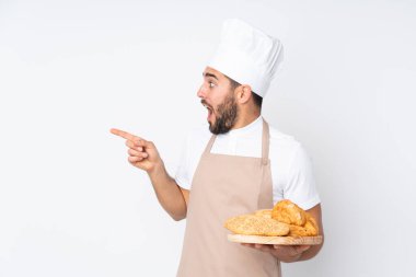 Erkek fırıncı, beyaz arka planda izole edilmiş birkaç ekmeği olan bir masa tutuyor.