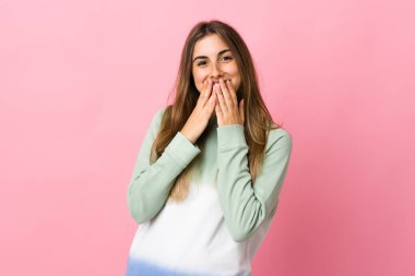 Soyutlanmış pembe arka planda genç bir kadın mutlu ve gülümsüyor elleriyle ağzını kapatıyor.