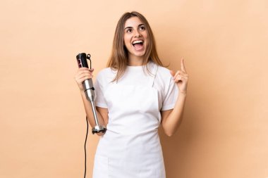 İzole edilmiş arka plan üzerinde el blenderi kullanan kadın yukarı ve şaşırmış