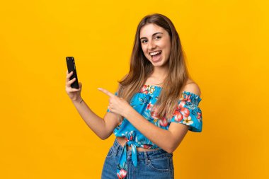 İzole edilmiş sarı arka plan üzerinde cep telefonu kullanan genç bir kadın.