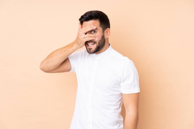 Beyaz tenli yakışıklı adam bej arka planda izole edilmiş gözleri elleriyle kapamış ve gülümsüyor.