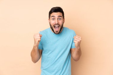 Beyaz tenli yakışıklı adam bej arka planda izole edilmiş ve galibiyeti kutluyor.