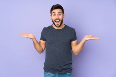 İzole edilmiş mor arka plan üzerinde şok olmuş yüz ifadesi olan beyaz yakışıklı bir adam.