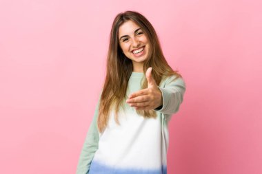 Soyutlanmış pembe arka planda genç bir kadın iyi bir anlaşma için el sıkışıyor.