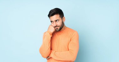 İzole edilmiş mavi arka planda yorgun ve sıkılmış bir ifadeye sahip beyaz yakışıklı bir adam.