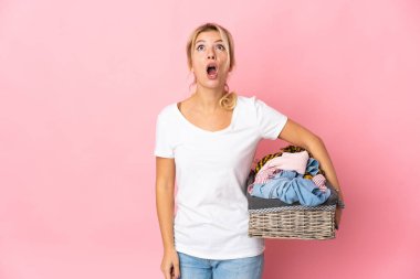 Pembe arka planda izole edilmiş çamaşır sepetini tutan genç Rus kadın yukarı bakıyor ve şaşırmış bir ifadeyle