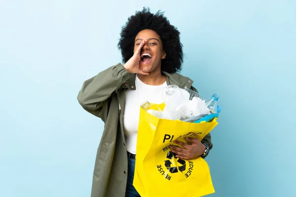 Young African American woman holding a recycle bag isolated on colorful background shouting and announcing something