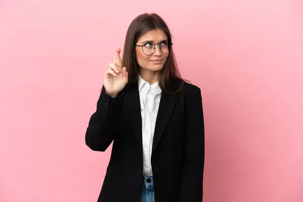 Young Business caucasian woman isolated on pink background with fingers crossing and wishing the best