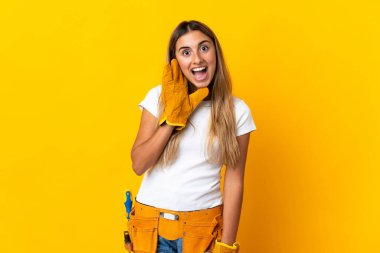 Genç İspanyol elektrikçi kadın, şaşırmış ve şok olmuş bir yüz ifadesiyle izole edilmiş sarı duvarın üzerinde.