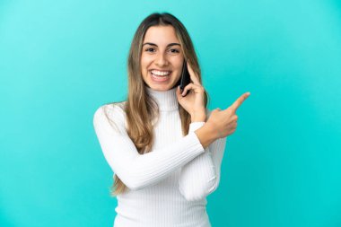 Mavi arka planda izole edilmiş cep telefonu kullanan beyaz bir kadın bir ürünü sunmak için yan tarafı işaret ediyor.