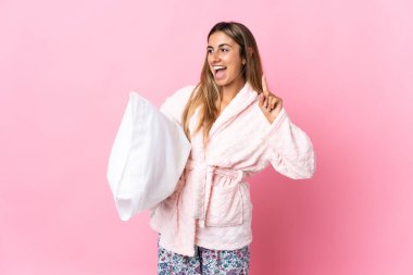 Genç İspanyol kadın, pijamalarıyla pembe arka planda izole edilmiş ve parmağını kaldırarak çözümü bulmaya çalışıyor.