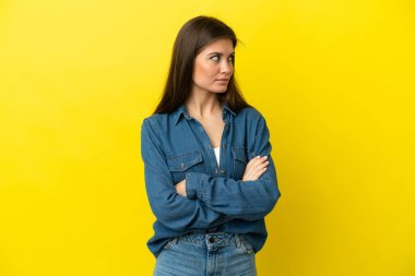 Sarı arka planda izole edilmiş genç beyaz kadın kollarını kavuşturuyor.