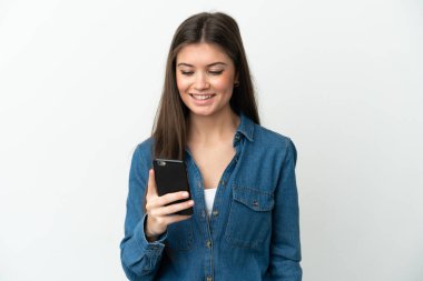 Beyaz arka planda izole edilmiş genç beyaz kadın cep telefonuyla mesaj ya da e-posta gönderiyor.