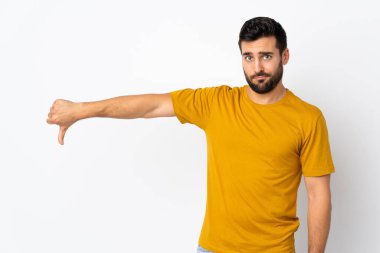 Beyaz arka planda sakallı yakışıklı genç adam olumsuz bir ifadeyle baş parmağını aşağı gösteriyor.