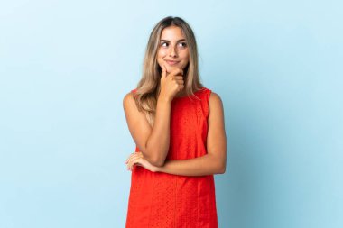Soyutlanmış mavi arka planda genç İspanyol kadın bir fikir düşünürken yukarı bakıyor.