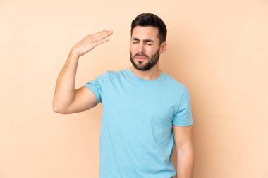 Beyaz tenli yakışıklı adam bej arka planda izole edilmiş, yorgun ve hasta bir ifadesi var.