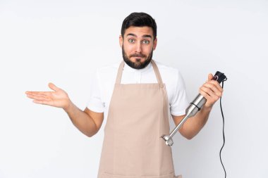 Beyaz arkaplanda izole edilmiş el blenderi kullanan adamın yüz ifadesi ile ilgili şüpheleri var