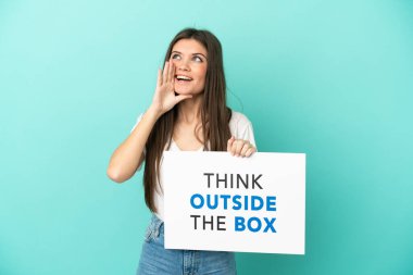 Kafkasyalı genç bir kadın mavi arka planda izole edilmiş. Elinde yazılı bir levha var. Kutunun Dışını Düşün ve bağır.