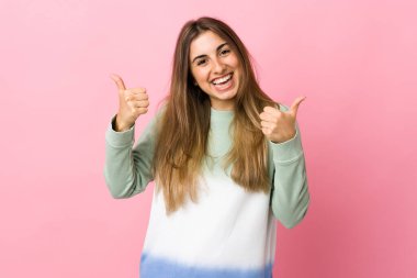 Soyutlanmış pembe bir geçmişi olan genç bir kadın. Baş parmakları havada ve gülümsüyor.