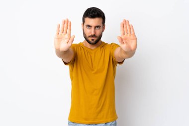 Beyaz arka planda sakallı yakışıklı genç adam dur hareketi yapıyor ve hayal kırıklığına uğruyor.