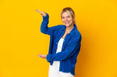 Sarı arka planda izole edilmiş genç bir Rus kadın ilan vermek için kopyalama alanı tutuyor.