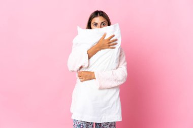 Pijamalı ve elinde yastıkla soyutlanmış pembe arka planda genç bir İspanyol kadın.