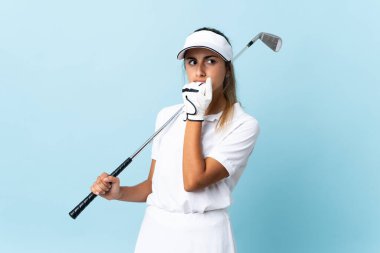 İzole edilmiş mavi duvarın üzerinde kuşkuları olan genç bir İspanyol golfçü kadın.