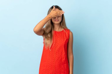 İzole edilmiş mavi arka planda genç İspanyol kadın gözlerini elleriyle kapatıyor. Bir şey görmek istemiyorum.