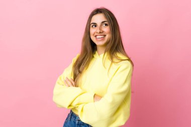 Soyutlanmış pembe arka planı olan genç bir kadın gülümserken yukarı bakıyor.