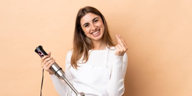 İzole arka planda el blenderi kullanan kadın para hareketi yapıyor