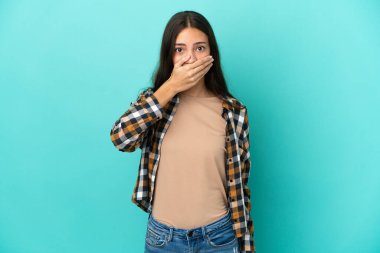 Genç bir Fransız kadın, mavi arka planda izole edilmiş, ağzı elle kapatılmış.