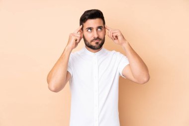 Beyaz tenli yakışıklı adam bej arka planda izole edilmiş. Şüpheleri ve düşünceleri var.