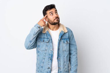 Beyaz arka planda sakallı genç ve yakışıklı bir adam deliliğin jestini yapıyor. Parmağını kafasına koyuyor.