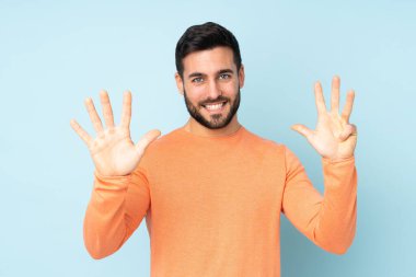 Beyaz tenli yakışıklı dokuz kişi sayıyor. Parmakları izole edilmiş mavi arka planda.