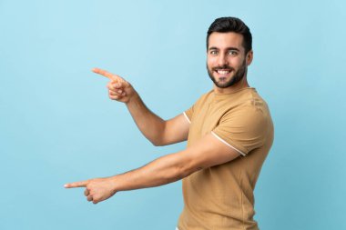 Arka planda sakallı, yakışıklı genç bir adam parmak kaldırıyor ve bir ürün sunuyor.