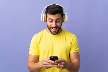 Mor arka planda sakallı yakışıklı genç adam müzik dinliyor ve hareketli bir şeyler arıyor.