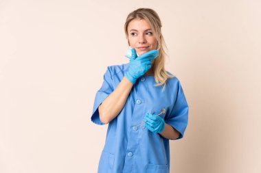 Dişçi kadın, izole bir arka plan üzerinde araçlar tutarak bir fikir düşünüyor