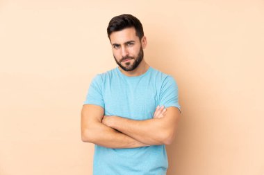 Beyaz tenli yakışıklı adam bej arka planda izole edilmiş üzgün hissediyor.