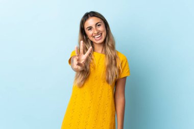 İzole edilmiş mavi arka planda yaşayan genç İspanyol kadın mutlu ve parmaklarıyla üçe kadar sayıyor.