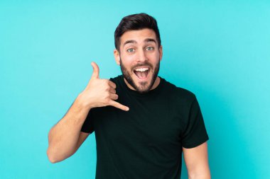 Beyaz, yakışıklı bir adam mavi arka planda izole edilmiş, telefon jesti yapıyor. Bana geri dönüş işareti ver.