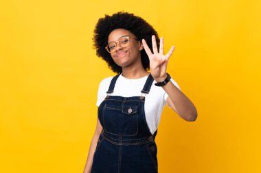 Sarı arka planda izole edilmiş genç Afrikalı Amerikalı kadın mutlu ve parmaklarıyla dört tane sayıyor.