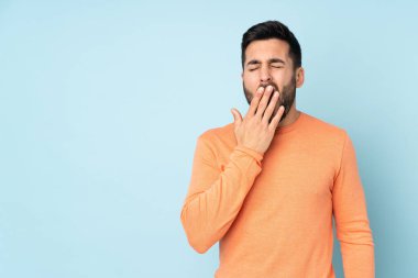 Beyaz tenli yakışıklı adam esniyor ve ağzı açık, elleri izole edilmiş mavi arka planda.