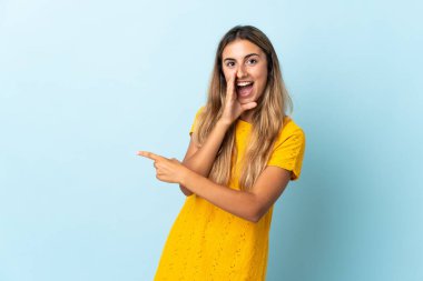 Tecrit edilmiş mavi arka planda genç bir İspanyol kadın bir ürünü sunmak ve bir şeyler fısıldamak için kenarı işaret ediyor.