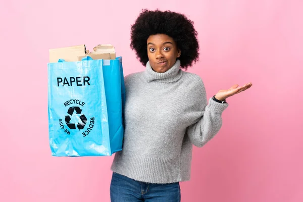 年轻的非洲裔美国女人拿着一个用五颜六色的背景隔离的回收袋 一边举手一边怀疑 — 图库照片