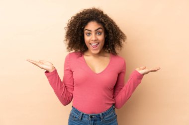 Genç Afrikalı Amerikalı kadın bej arka planda izole edilmiş ve şok olmuş bir yüz ifadesi var.