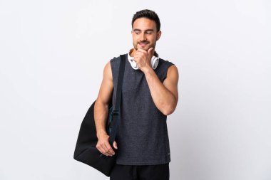 Spor çantalı genç adam beyaz arka planda izole edilmiş, yana bakıyor ve gülümsüyor.